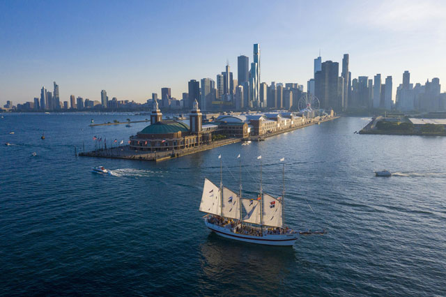 Aerial view of a sailboat sailing near a city skyline with a Ferris wheel.