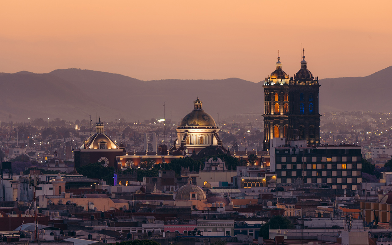 Lights appear around a 16th-century city as the sun sets