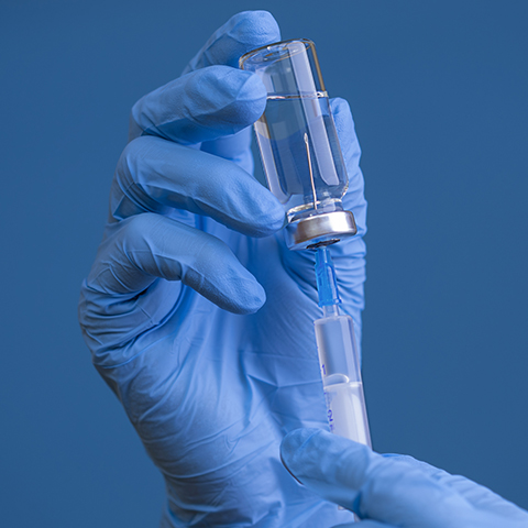 A gloved hand holds a vial and syringe against a blue background